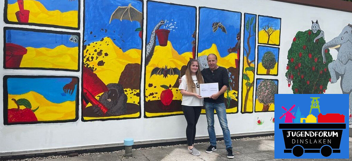 Pressefoto des Künstlers Gianni Düx und einer Mitarbeiterin des Jugendzentrums vor der Wand mit der fertigen Comiczeichnung.